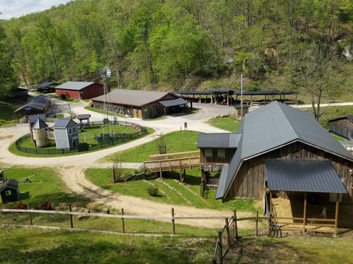 Heritage Farm Village and Museum seen from above, featuring wooden buildings, a red barn, and a steel windmill connected by gravel paths.