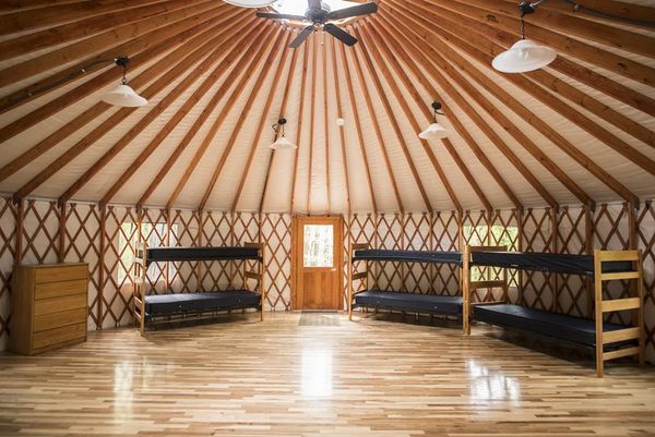The inside of a yurt, featuring sturdy wooden bunk beds, ceiling lights and a ceiling fan, and shining wood floors.