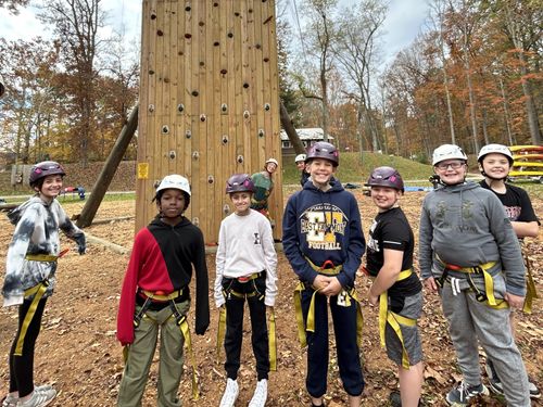 Students wearing helmets and harnesses smile in front of the climbing tower at Jacksons Mill.