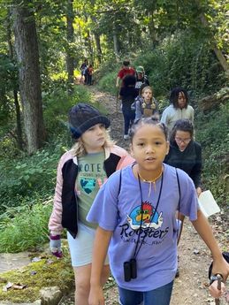 Students go on a hike through a forested section of the Farm, carrying binoculars and notebooks.