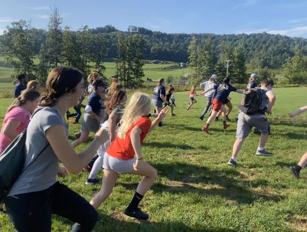 Students, staff, and a teacher run joyfully across a grassy field.