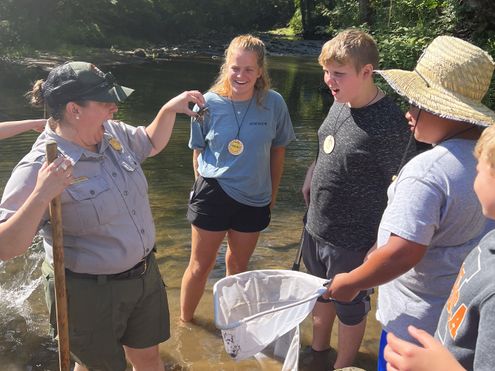 A New River Gorge park ranger holds up a crayfish for students to see, while standing in a shallow creek.