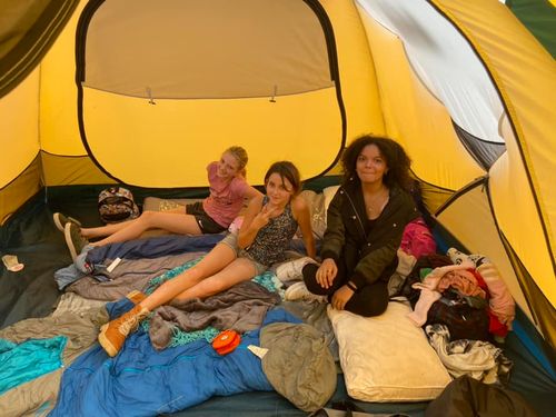 Three students sit inside their sleeping tent, which is spacious and tall, surrounded by their sleeping bags and personal gear.