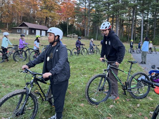 Students on mountain bikes line up for a ride. One student on a bike makes a funny face at the camera.