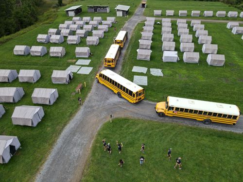 SAS campsite as seen from the air: Four school buses pull next to rows of gray canvas tents in a grassy field.