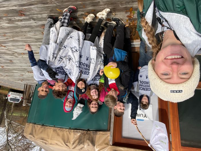 Happy students wear SAS t-shirts and wave their group's flag in this selfie, taken by their SAS instructor, in front of a yurt.