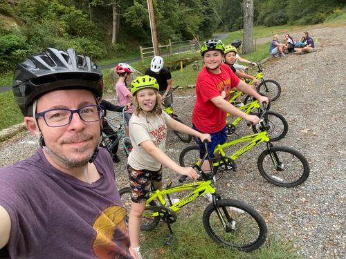 A teacher and his students pose for a picture during BMX biking class, wearing helmets and holding bright yellow bikes.