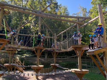 Students wearing Science Adventure School t-shirts climb on a two-level, wooden challenge course, featuring wooden bridges and ropes.