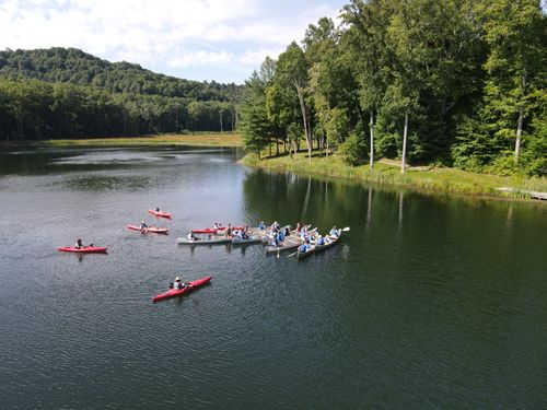 Students and staff float in canoes and kayaks on Goodrich Lake at the Summit, surrounded by green hills.